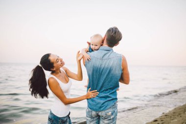 güzel genç aile bebek ile tatilde. Babası sarışın kız onun kollarında tutar ve kumral'ın anne kocası sarılarak. Aile plaj tatil yaz denize yakın kavramı