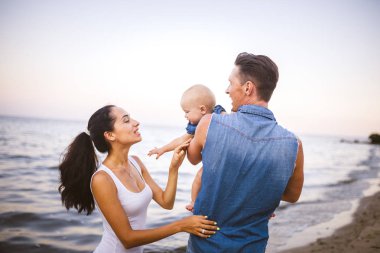 güzel genç aile bebek ile tatilde. Babası sarışın kız onun kollarında tutar ve kumral'ın anne kocası sarılarak. Aile plaj tatil yaz denize yakın kavramı