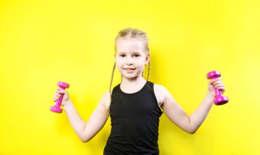 Tema spor ve sağlık. Gülümseme ile sarı arka plan üzerinde poz pigtails kız güzel çocuk. küçük atlet holding pembe dambıl. Banner reklam, metin kopya alanı alan için