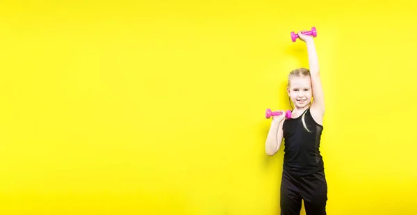 Tema deporte y salud. Hermosa niña caucásica con coletas posando sobre fondo amarillo con sonrisa. Pequeño atleta sosteniendo pesas rosas. Banner para publicidad, espacio para espacio de copia de texto — Foto de Stock