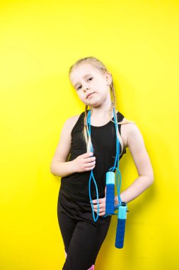 Tema spor ve sağlık. Gülümseme ile sarı arka plan poz pigtails kız güzel çocuk. küçük atlet spor ipi elinde tutar. Banner reklam, metin kopya alanı boş alan