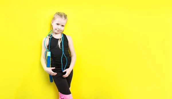 Θέμα Αθλητισμός και υγεία. Όμορφο Καυκάσιος παιδί κορίτσι με κοτσίδες θέτοντας κίτρινο φόντο με χαμόγελο. λίγο αθλητής κατέχει το άθλημα σχοινί στα χέρια. Banner διαφήμιση, χώρο για διάστημα αντίγραφο κείμενο κενό — Φωτογραφία Αρχείου