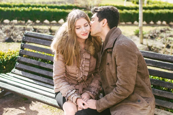 Jeune couple multiracial, étudiants hétérosexuels masculins et féminins amoureux. Un rendez-vous dans un parc municipal sur un banc en bois. Jeune homme brune à la peau foncée et une femme caucasienne dans une étreinte par une journée ensoleillée — Photo