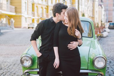 Genç çift çok ırklı, erkek ve kadın aşık heteroseksüel insanların öğrenciler. Güzel modeller ayakta poz retro bir araba şehrin yakınlarında. Giymiş siyah elbise