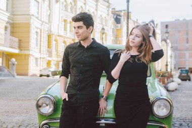 Genç çift çok ırklı, erkek ve kadın aşık heteroseksüel insanların öğrenciler. Güzel modeller ayakta poz retro bir araba şehrin yakınlarında. Giymiş siyah elbise