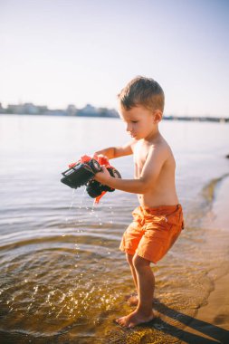 Konu inşaat ve ağır sanayi. Soyutlama çocuk çocuk yaz oyuncak kırmızı traktör modeli nehirde, bir kova ile tarak makine yakınındaki kum oynamak