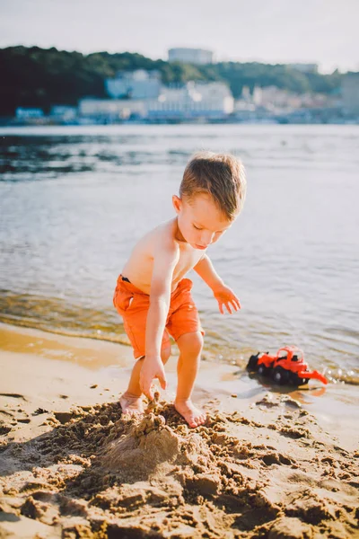 Sujet construction et industrie lourde. Abstraction enfant garçon jouant sur le sable près de la rivière dans le modèle de tracteur rouge jouet d'été, excavatrice avec un seau — Photo
