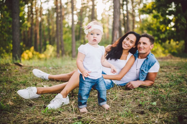 Petite fille un an sur le fond des parents reposant sur l'herbe apprenant à marcher sur la nature dans le parc. Les premiers pas d'un enfant dans la nature en dehors de la ville dans la forêt — Photo