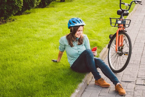 Denek ekolojik ulaşım bisikleti. Mavi kasklı, uzun saçlı, turuncu renkli bir bisikletin yanında duran, şehir parkında sepeti olan güzel, beyaz bir kadın. — Stok fotoğraf