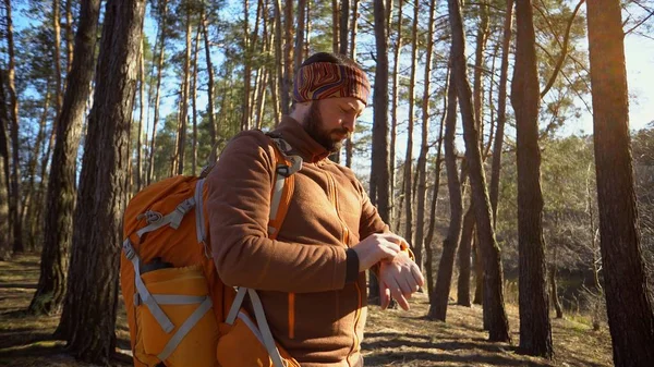 Je čas cestovat a dobrodružství. Portrét poutníka z vousatého muže, s batohu, používá technologické sportovní hodinky pro navigaci GPS elektronického kompasu v lese a dívá se na hodinky — Stock fotografie