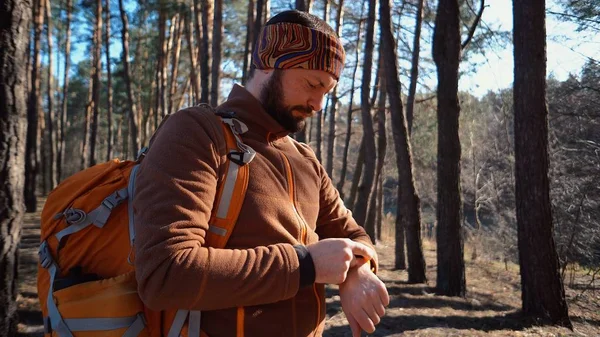 Llegue a tiempo en viajes y aventuras. Cintura hacia arriba retrato de hombre barbudo viajero, con mochila, utiliza tecnología reloj deportivo para navegar gps brújula electrónica en el bosque y mirando su reloj — Foto de Stock