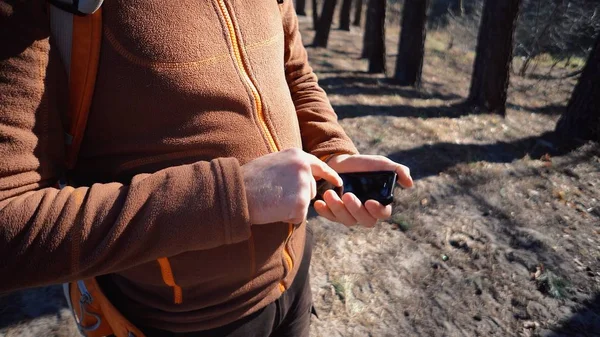 テーマ観光とテクノロジー。あごひげとバックパックを持つ若い白人男性。松の森でのハイキングの観光客は、画面をタッチする携帯電話を保持し、技術を使用しています。Gps アプリケーションの向き — ストック写真