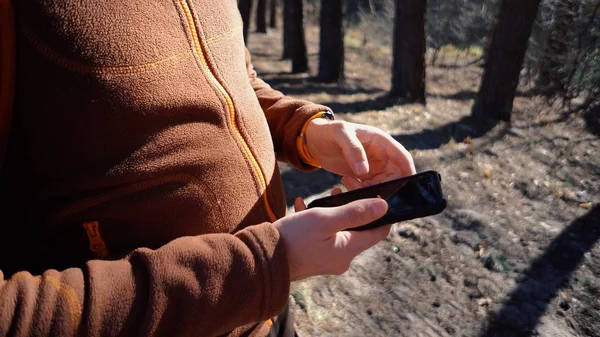 Turismo temático y tecnología. Joven hombre caucásico con barba y mochila. Senderismo turista en bosque de pinos utiliza la tecnología, la mano celebración de teléfono móvil para tocar la pantalla. Orientación de la aplicación Gps — Foto de Stock