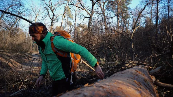 Een jonge mannelijke toerist met een rugzak stappen over een omgevallen boom in het bos met een rugzak. Thema wandelen Toerisme in het bos. Moeilijkheden en uitdagingen overwinnen — Stockfoto