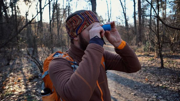 Turista viajero turista hombre caucásico con barba y una mochila mirando a través de la vergonzosa tubería en el paisaje de la naturaleza en el bosque. Un turista mira la vida silvestre en el telescopio — Foto de Stock