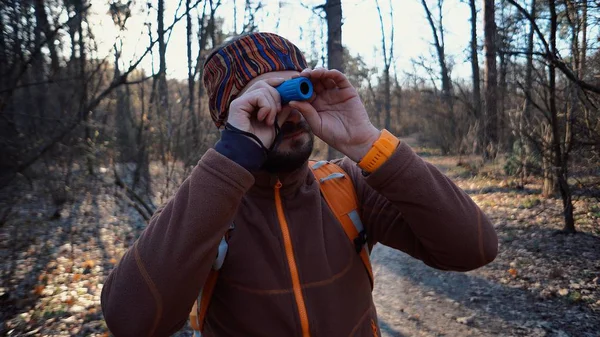 Turysta turysta turystyczny kaukaski człowiek z brodą i plecak patrząc przez haniebne rury na krajobraz przyrody w lesie. Turysta patrzy na przyrodę w teleskopie — Zdjęcie stockowe