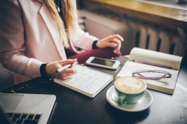 Kafeteryanın içindeki ahşap masaya beyaz kadın elini koy ve not defterine not al. Denek serbest yazar blogcu gazeteci iş başında. Tanımlanamayan kişi. Teknoloji telefonu ve fincan kahveli dizüstü bilgisayar.