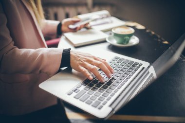 Beyaz kadının elleriyle yakın yukarı görünümü CAS, öğrenci, Blogger, yazar adam elinde bir telefon tutan bir dizüstü bilgisayar üzerinde çalışan, kafe içinde ahşap bir masa ve bir fincan kahve