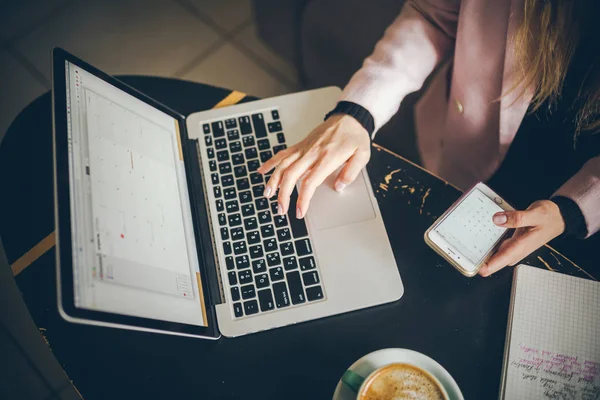 Beyaz kadının elleriyle yakın yukarı görünümü CAS, öğrenci, Blogger, yazar adam elinde bir telefon tutan bir dizüstü bilgisayar üzerinde çalışan, kafe içinde ahşap bir masa ve bir fincan kahve — Stok fotoğraf