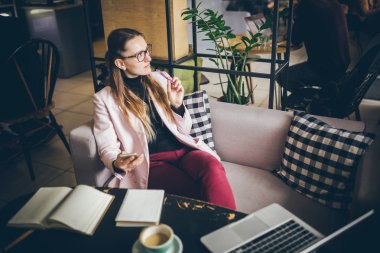 Tema modern meslek kadın Blogger. Gözlük ve ceket ile ahşap masa arkasındaki kahve dükkanında oturan beyaz kadın Notebook, dizüstü bilgisayar ve fincan kahve. Kız duygu rüya, yazar düşünüyorum