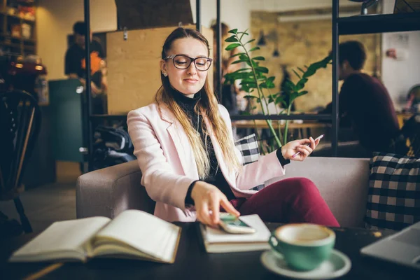 Tema modern meslek kadın Blogger. Gözlük ve ceket ile ahşap masa arkasındaki kahve dükkanında oturan beyaz kadın Notebook, dizüstü bilgisayar ve fincan kahve. Kız duygu rüya, yazar düşünüyorum