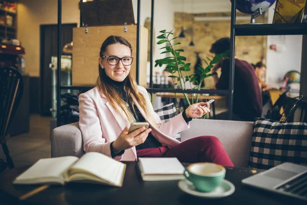 Θέμα μοντέρνο επάγγελμα θηλυκό blogger. Καυκάσια γυναίκα με γυαλιά και μπουφάν που κάθονται μέσα στην καφετέρια πίσω από ξύλινο τραπέζι με φορητό υπολογιστή, laptop και φλιτζάνι καφέ. Κορίτσι συναίσθημα όνειρο, σκεφτείτε συγγραφέα — Φωτογραφία Αρχείου