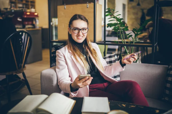 Tema profissão moderna blogueiro feminino. Mulher caucasiana com óculos e jaqueta sentada dentro da cafetaria atrás da mesa de madeira com notebook, laptop e xícara de café. Menina sonho emoção, pensar escritor — Fotografia de Stock