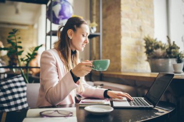 Güzel genç beyaz kadın kahve içme ve ahşap bir masada bir kafe içinde bir klavyede yazarak. Modern mesleklerin konu bir Blogger, Freelancer ve yazar olduğunu
