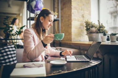 Güzel genç beyaz kadın kahve içme ve ahşap bir masada bir kafe içinde bir klavyede yazarak. Modern mesleklerin konu bir Blogger, Freelancer ve yazar olduğunu