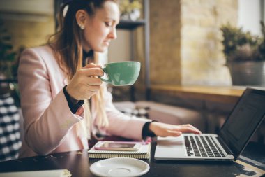 Güzel genç beyaz kadın kahve içme ve ahşap bir masada bir kafe içinde bir klavyede yazarak. Modern mesleklerin konu bir Blogger, Freelancer ve yazar olduğunu