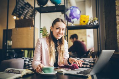 Güzel genç beyaz kadın kahve içme ve ahşap bir masada bir kafe içinde bir klavyede yazarak. Modern mesleklerin konu bir Blogger, Freelancer ve yazar olduğunu