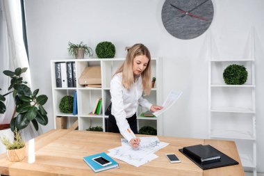 Tema iş kadını iş başında. Güzel genç kafkas kadın iş adamı çalışma ayakta tablo yakınındaki ofiste denetler kağıt üzerinde düzenlemeler finansal grafikler