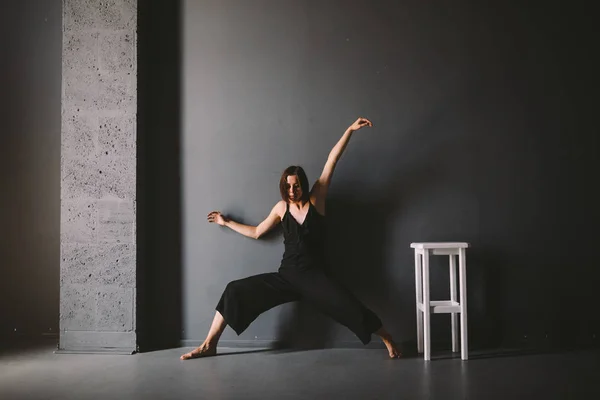 O tema social da solidão feminina é o sofrimento da dor. Abastração da violência doméstica masculina. Mulher branca bonita nova na roupa preta, pose estranha, quarto escuro grande da cadeira branca. Medo e desespero — Fotografia de Stock