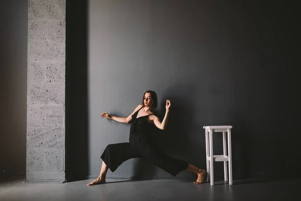 O tema social da solidão feminina é o sofrimento da dor. Abastração da violência doméstica masculina. Mulher branca bonita nova na roupa preta, pose estranha, quarto escuro grande da cadeira branca. Medo e desespero — Fotografia de Stock