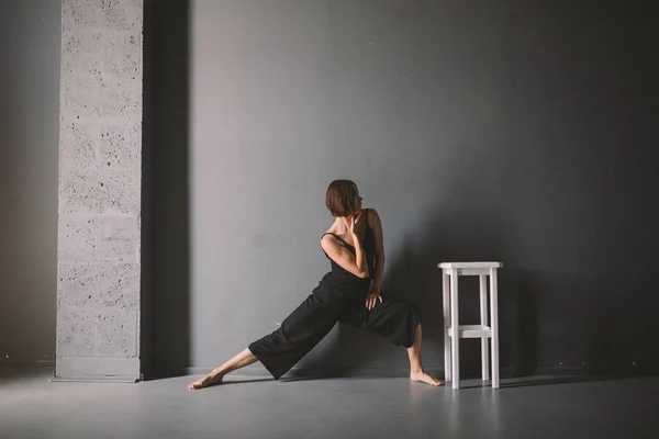 O tema social da solidão feminina é o sofrimento da dor. Abastração da violência doméstica masculina. Mulher branca bonita nova na roupa preta, pose estranha, quarto escuro grande da cadeira branca. Medo e desespero — Fotografia de Stock