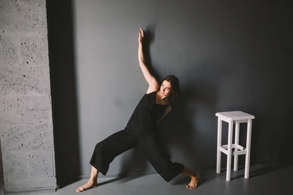 Le thème social de la solitude féminine est la souffrance. Abastration de la violence domestique masculine. Jeune belle femme caucasienne en vêtements noirs, pose étrange, chaise blanche grande chambre sombre. Peur et désespoir — Photo