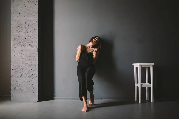 O tema social da solidão feminina é o sofrimento da dor. Abastração da violência doméstica masculina. Mulher branca bonita nova na roupa preta, pose estranha, quarto escuro grande da cadeira branca. Medo e desespero — Fotografia de Stock