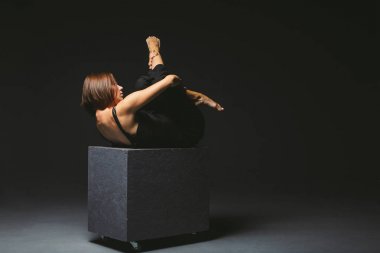 Sosyal tema. siyah küp üzerinde poz elbise garip poz genç kafkas kadın, karanlık arka plan, ağrı sembolize, acı, yardım isteyen, kötü bir toplumun korunması. Modern sanat, soyutlama