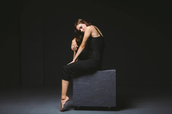 Tema social. jovem mulher caucasiana em pose estranha em vestido posando no cubo preto, fundo escuro, simboliza dor, sofrimento, buscando ajuda, proteção de uma sociedade má. Arte moderna, abstração — Fotografia de Stock