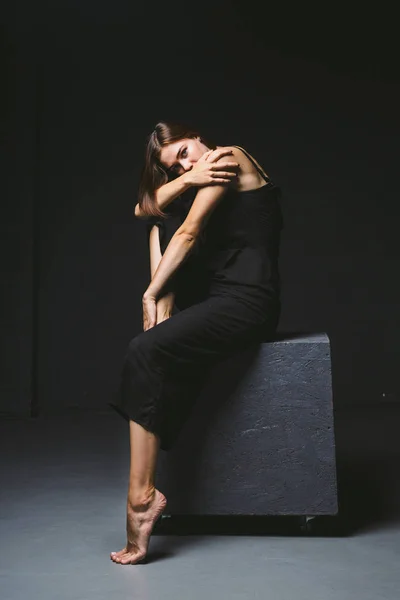 Tema social. jovem mulher caucasiana em pose estranha em vestido posando no cubo preto, fundo escuro, simboliza dor, sofrimento, buscando ajuda, proteção de uma sociedade má. Arte moderna, abstração — Fotografia de Stock