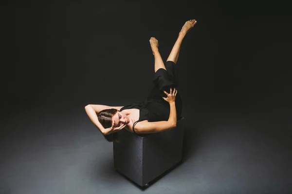 Tema social. joven mujer caucásica en pose extraña en vestido posando sobre cubo negro, fondo oscuro, simboliza el dolor, el sufrimiento, la búsqueda de ayuda, la protección de una sociedad malvada. Arte moderno, abstracción — Foto de Stock