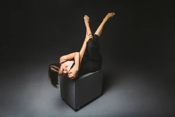 Tema social. joven mujer caucásica en pose extraña en vestido posando sobre cubo negro, fondo oscuro, simboliza el dolor, el sufrimiento, la búsqueda de ayuda, la protección de una sociedad malvada. Arte moderno, abstracción — Foto de Stock