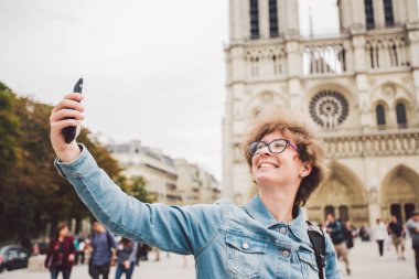 Paris'te Turist Notre Dame Katedrali yakınında komik selfie yapıyor. Paris'te sırt çantası ile güzel genç beyaz turist kadın komik selfie el tutan telefon yapma, Notre Dame Katedrali yakınında fotoğraf
