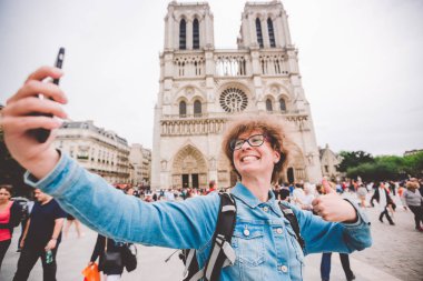 Paris'te Turist Notre Dame Katedrali yakınında komik selfie yapıyor. Paris'te sırt çantası ile güzel genç beyaz turist kadın komik selfie el tutan telefon yapma, Notre Dame Katedrali yakınında fotoğraf