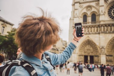 Paris'te turist, Notre Dame Katedrali'nin fotoğrafını çekiyor. Paris'te bir sırt çantası ile Eller Kafkas kadın turist, el cep telefonu teknolojisi kullanır fotoğraf video cazibe Notre Dame yapar