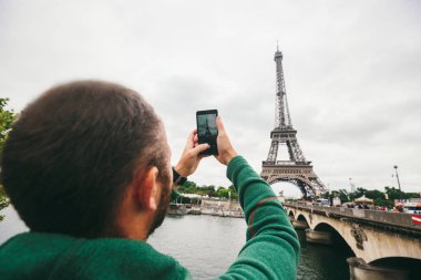 Eller Kafkas erkek turist blogger akıllı telefon kullanarak en önemli manzaraları Paris Fransa Eyfel Kulesi fotoğraf yapar