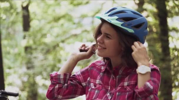 Subject ecological mode of transport bicycle. Beautiful young Caucasian woman wearing a blue helmet and long hair poses standing next to an orange-colored rental bike with a basket in a city park — Stock Video