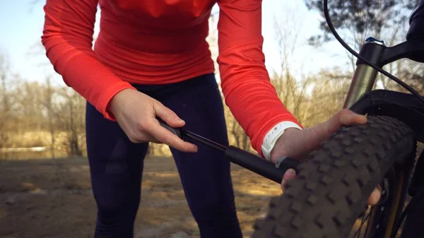 Young caucasian woman athlete tourist cyclist uses a hand tool, a bicycle pump to inflate air into a tire wheel mountain bike. Breakdown and quick repair of a bicycle in the countryside outside — ストック写真