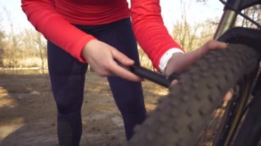 Genç beyaz kadın sporcu turist bir el aleti kullanıyor, bisiklet pompası tekerlek dağ bisikletine hava pompalamak için. Çöküş ve kırsal alanda hızlı bir bisiklet tamiri.
