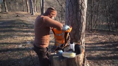 Tema yürüyüş ve seyahat. Bir Kafkas turist adam turuncu bir sırt çantası ayıklar, onun eşyalarını alır ve ormanda bir kütüğe koyar. Kamp için ekipman ve şeyler